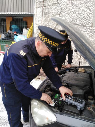 Funkcjonariusz Straży Miejskiej pomaga uruchomić pojazd korzystając z urządzenia rozruchowego