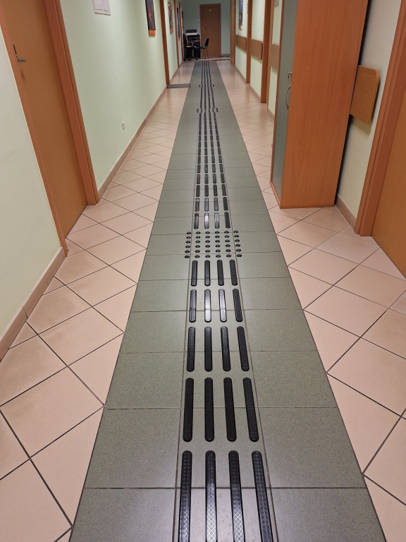 Korytarz budynku Urzędu Miasta Rzeszowa przy ul.  Okrzei 1 z poziomym oznaczeniem informacyjno-dotykowym ułatwiającym orientację  osobom z niepełnosprawnością wzroku